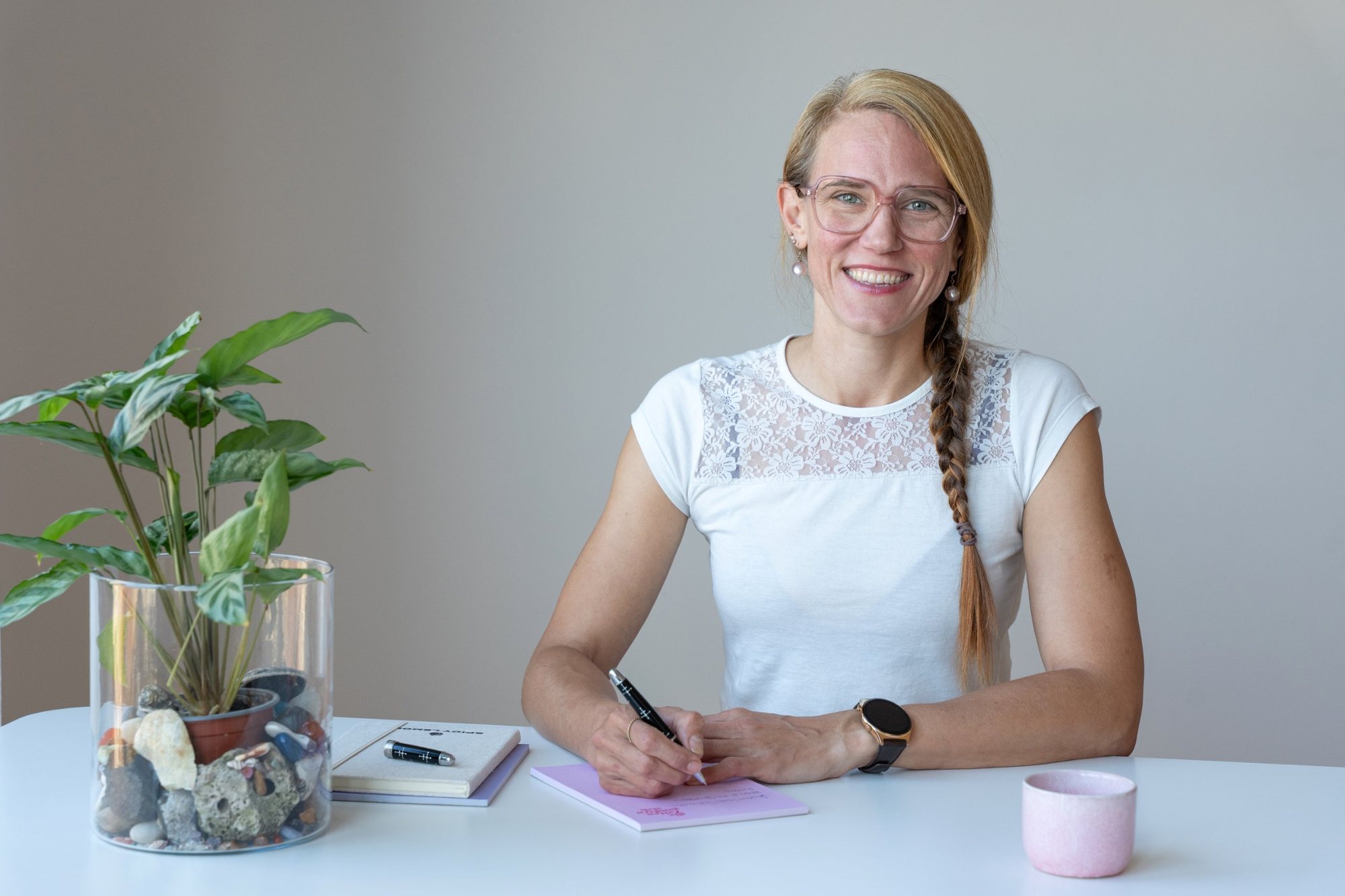 Patricia sitzt lächelnd am Tisch und macht sich Notizen