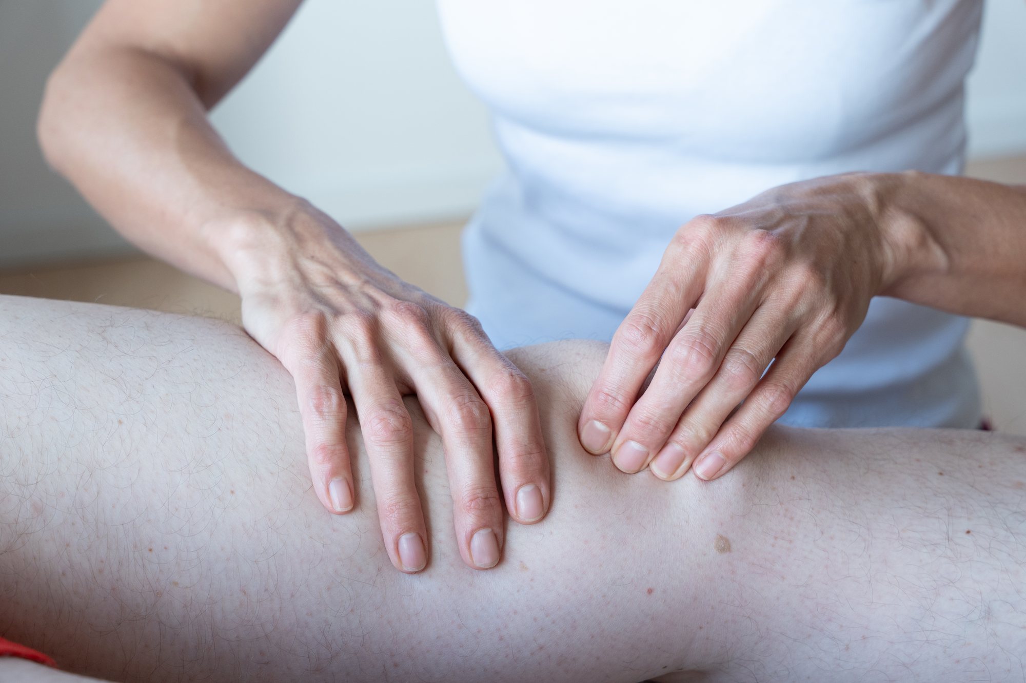 Hände ertasten das Gewebe am Knie