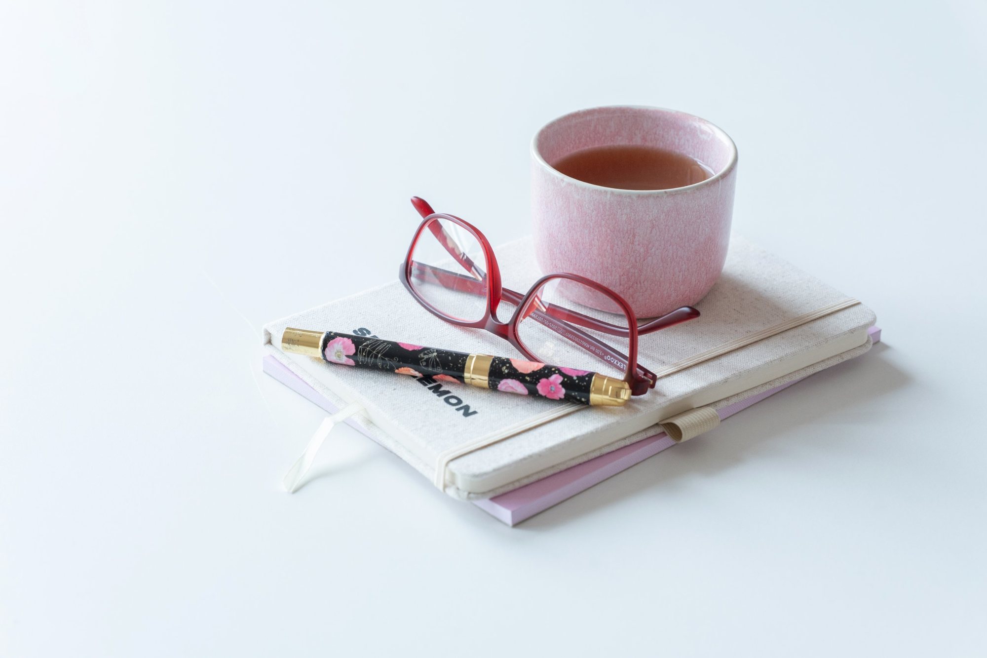 Rosa Teetasse auf einem Notizbuch mit Füller